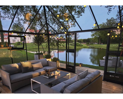 Gewächshaus mit Sitzgruppe, Tisch und Beleuchtung mit Blick auf einen See