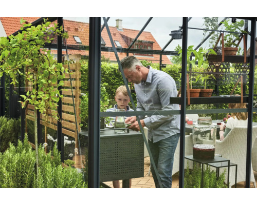 Familie in einem Gewächshaus mit Pflanzen und Gartenmöbeln.
