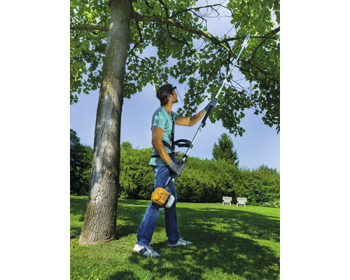 Mann mit Gesichtsschutz und Trimmer beim Beschneiden eines Baumes im Garten.
