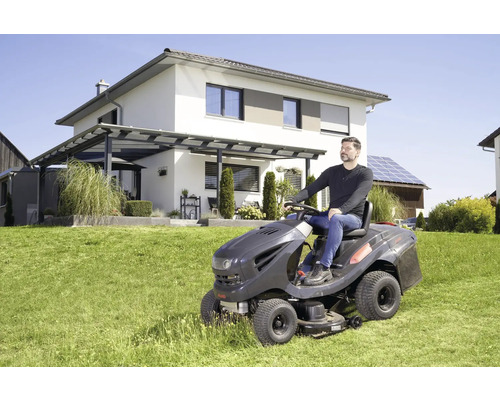 Mann auf Rasentraktor beim Rasenmähen vor einem Wohnhaus