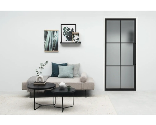 Helles Wohnzimmer mit Sofa, Couchtischen, Pflanzenbildern und einer Tür mit Glaseinsatz.