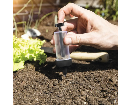 Person verwendet Dosierhilfe für Saatgut im Gartenbeet