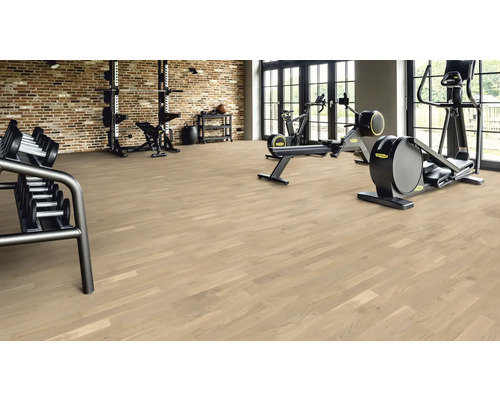 Fitnessraum mit Holzboden, Hanteln und Trainingsgeräten.