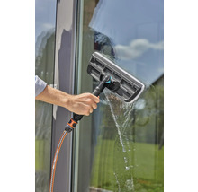 Eine Person reinigt ein Fenster mit einem Fensterwischer und einem Wasserschlauch.
