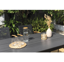 Gartenszene mit Tisch, Stühlen, Gläsern, Wasserkaraffe, Kerze und Dekoration.