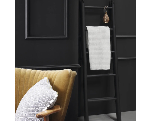 Szene mit Leiter als Handtuchhalter, Handtuch, Sessel und dekorativen Elementen vor dunkler Wand