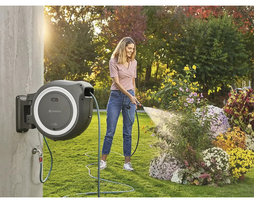 Frau bewässert Blumen mit einer an der Wand montierten Schlauchtrommel von Gardena im Garten.