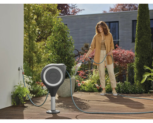 Gartenszene mit Frau, die einen Gartenschlauch aus einer Schlauchbox mit Ständer verwendet