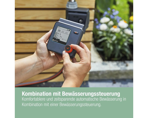 Eine Person bedient eine Gardena Bewässerungssteuerung im Garten.