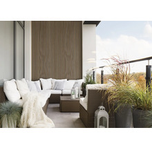 Balkon mit Rattansitzgruppe, Kissen, Decke, Laternen und Pflanzenkübeln.