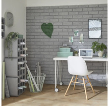 Arbeitszimmer mit Schreibtisch, Stuhl, Regalen und Dekorationsartikeln vor einer grauen Backsteinwand