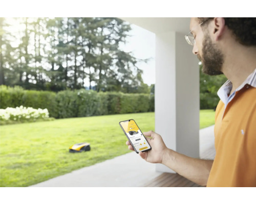 Mann bedient einen Rasenroboter mit einer Smartphone-App im Garten.