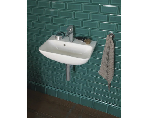 Waschbecken mit Armatur, Seifenschale und Handtuch vor gefliester Wand