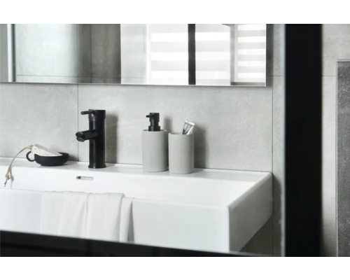 Waschbecken mit Armatur, Seifenspender und Zahnputzbecher im Badezimmer.