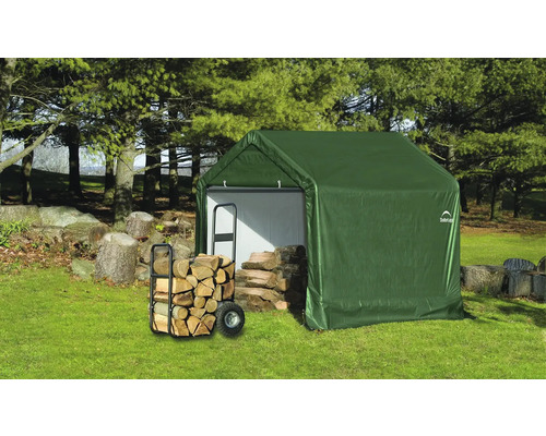 Grünes Gerätehaus mit Brennholz und Wagen im Garten.