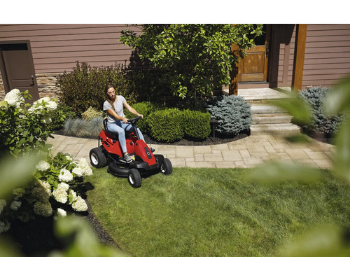 Frau fährt Rasentraktor auf Rasenfläche in einem Garten.