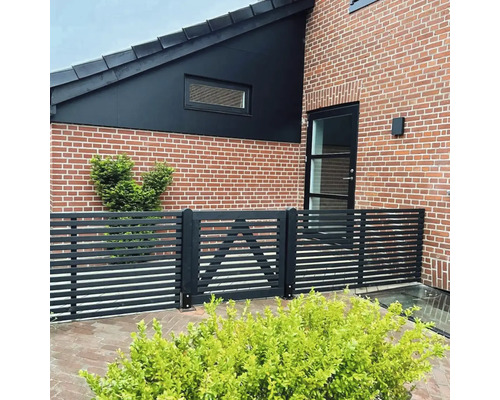 Außenansicht eines Hauses mit Backsteinfassade und einem Zaun mit Tor.