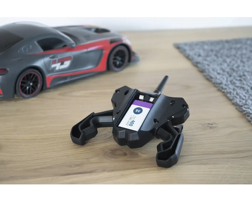 Schwarze Fernbedienung mit eingesetzter 9V-Batterie und Spielzeugauto im Hintergrund