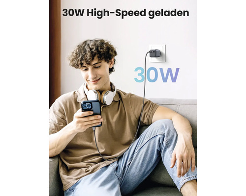 Ein junger Mann sitzt auf einem Sofa und benutzt ein Smartphone, das mit einem 30-Watt-Ladegerät verbunden ist.