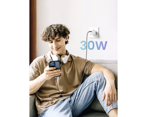 Ein Mann sitzt mit Kopfhörern auf der Couch und lädt sein Mobiltelefon mit einem 30-Watt-Ladegerät auf.