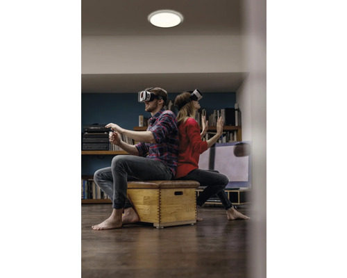 Mann und Frau sitzen Ruecken an Ruecken mit Virtual-Reality-Brillen auf einem Hocker