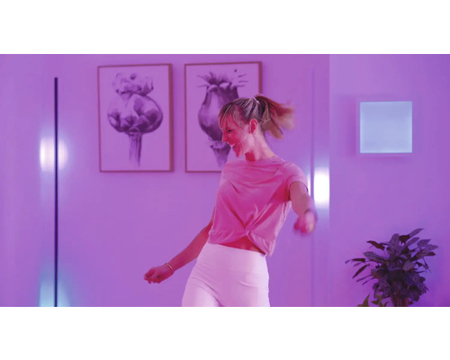 Frau tanzt in einem beleuchteten Raum mit Kunstwerken an den Wänden und Zimmerpflanzen.