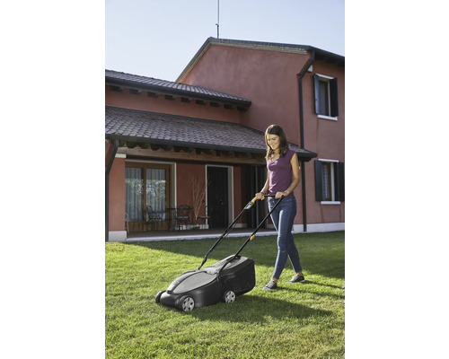 Frau benutzt einen Rasenmäher im Garten.