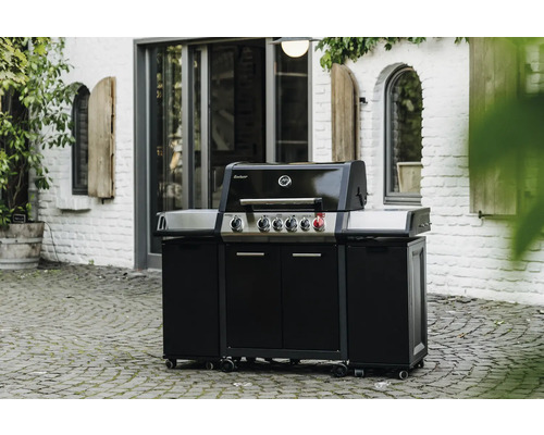 Schwarzer Gasgrill mit Unterschrank und Rädern im Außenbereich vor einem weißen Backsteingebäude.