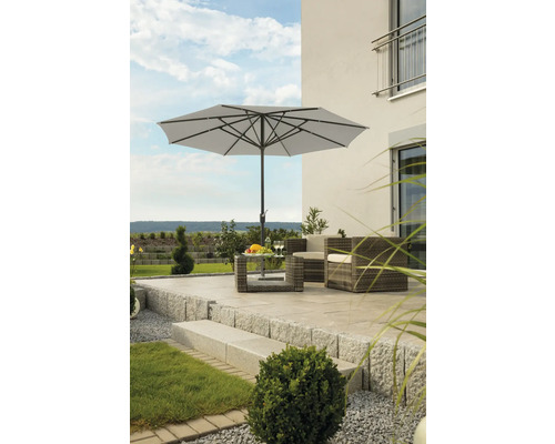 Gartenszene mit Sonnenschirm, Rattansitzgruppe und Tisch auf einer Terrasse