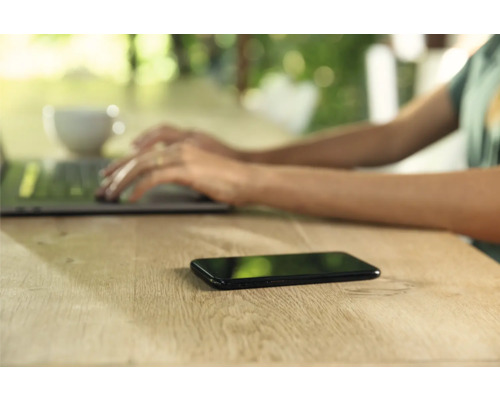 Smartphone auf Holztisch neben Laptop und Kaffeetasse