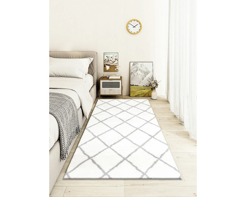 Schlafzimmer mit Bett, Nachttisch und weißem Teppich mit Rautenmuster