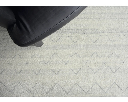 Detailaufnahme eines Teppichs mit geometrischem Muster und einem Stuhlbein