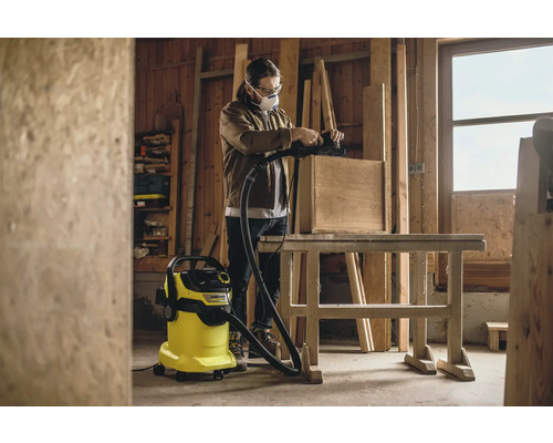 Handwerker schleift Holz mit Schleifgerät und Staubsauger in Werkstatt.