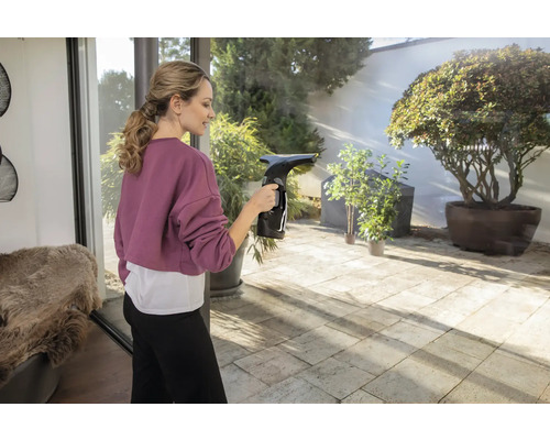 Frau reinigt Fenster mit einem Fenstersauger in einem hellen Raum