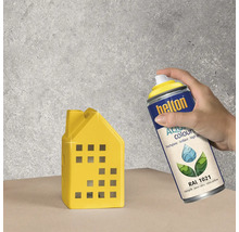 Eine Person sprüht ein gelbes Deko-Haus mit Helton Aqua Colours Sprühlack RAL 1021.