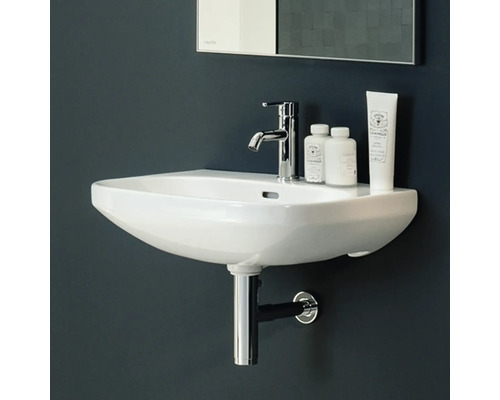 Keramikwaschbecken mit Armatur, Siphon und Kosmetikprodukten im Badezimmer.