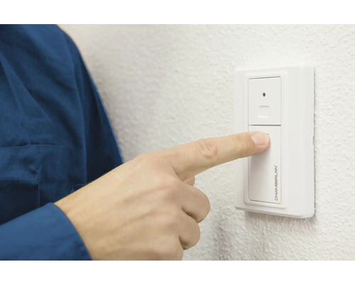 Eine Person betätigt einen Chamberlain Garagentoröffner-Wandschalter.