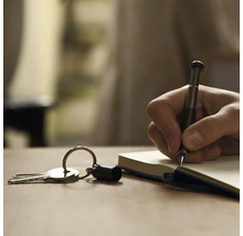 Eine Hand schreibt mit einem Stift in ein Notizbuch, neben einem Schlüsselbund.