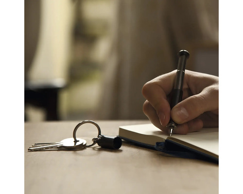 Eine Hand schreibt mit einem Stift in ein Notizbuch, neben einem Schlüsselbund.