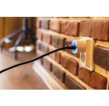 Steckdose mit eingestecktem Stecker an einer Ziegelwand