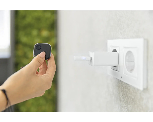 Eine Hand hält einen quadratischen Tracker, während ein Ladegerät in einer Steckdose steckt