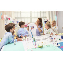 Gruppe von Kindern mit einer Frau, die ein selbstbemaltes T-Shirt mit einem Schmetterling hält, Bastelmaterialien auf einem Tisch