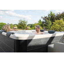 Personen entspannen in einem Whirlpool im Freien vor einer grünen Landschaft.