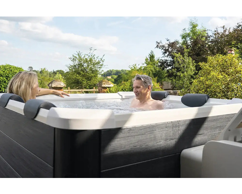 Personen entspannen in einem Whirlpool im Freien vor einer grünen Landschaft.