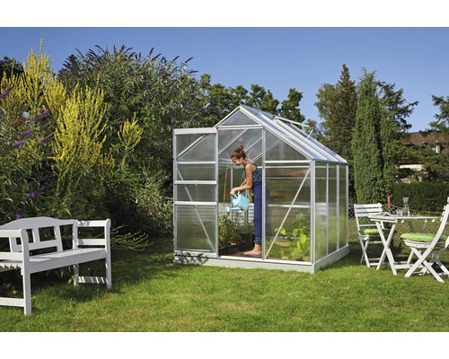 Gewächshaus im Garten mit Frau beim Gießen von Pflanzen