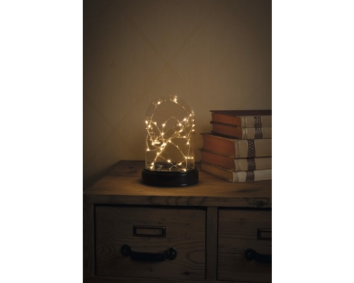 Dekorative Glaskuppel mit Lichterkette auf einem Nachttisch neben Büchern