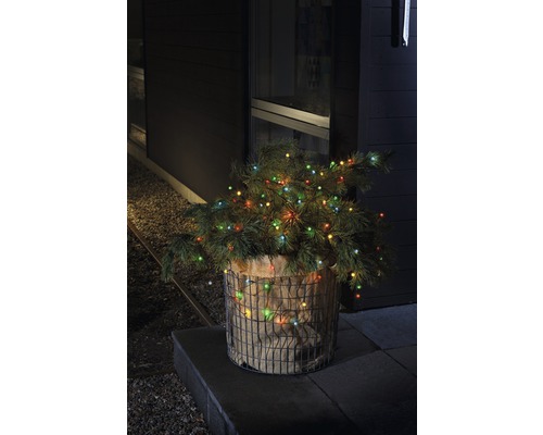 Dekorativer Weihnachtsbaum mit Lichtern in einem Drahtkorb vor einem Haus.