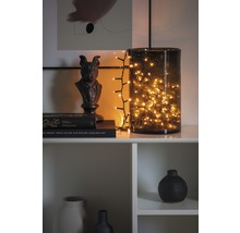 Dekoratives Arrangement mit Lichterkette in Glasvase, Skulptur und Büchern auf einem Regal