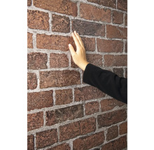 Eine Hand berührt eine rote Backsteintapete.