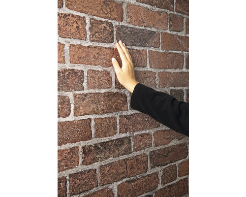 Eine Hand berührt eine rote Backsteintapete.